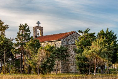 Güzel Arogi Ortodoks Kilisesi Karatza Gölü yakınlarında çam ağaçları ormanlarının arka bahçesiyle inşa edildi. Xanthi bölgesi, Kuzey Yunanistan. Tek zilli çan kulesi ve sonbahar günü bulutlu gökyüzü.