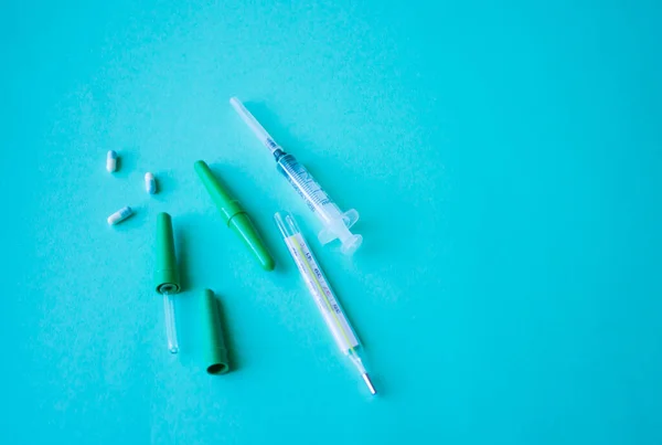 thermometer, syringe, medical containers lie on a mint-colored table, concept of patient care
