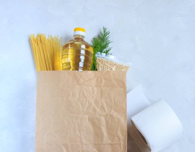 Masadaki pakette ayçiçeği yağı, inci arpası, tuvalet kağıdı, spagetti, otlar ve ev teslimatı konsepti var.