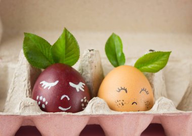 Üzerinde şirin boyalı bir yüz olan iki tavuk renkli yumurta, pembe arka planda bir yumurta kutusunda yatıyorlar, neşeli bir Paskalya konsepti.