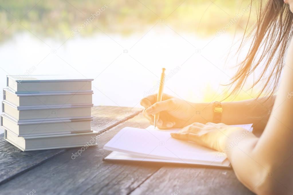 Stock Photo Woman right hand writing journal on small notebook at outdoor area with morning scene