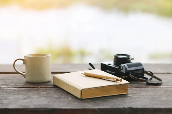 Склад Фото коричневая записная книжка с карандашом и кофейной чашкой, камера на гранж деревянный стол — стоковое фото