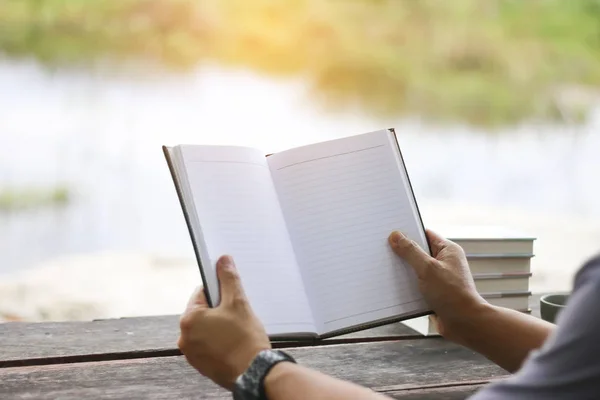 Ein junger Mann sitzt und liest ein Buch über den natürlichen Hintergrund — Stockfoto