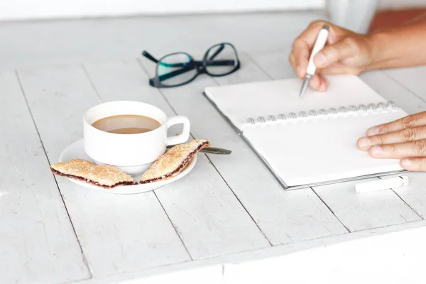 Foto di scorta Immagine ritagliata di un uomo seduto al tavolo in legno bianco vintage e caffè mentre lavorava con il blocco note — Foto Stock