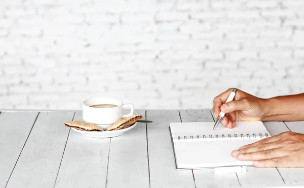 Stockfoto Cropped beeld van een man zit aan vintage witte houten tafel en de koffie tijdens het werken met Kladblok — Stockfoto