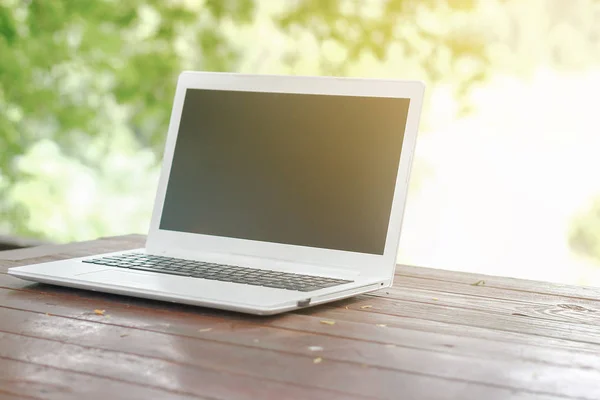 与空白背屏幕上的木桌和花园的绿色自然背景的股票照片电脑笔记本 — 图库照片