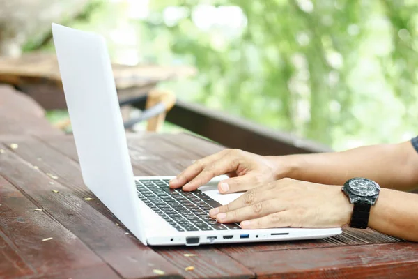 Photo de stock Gros plan vue à angle bas d'un homme travaillant sur un ordinateur portable assis sur une table en bois avec fond de nature flou Image En Vente