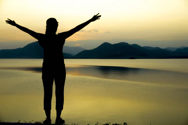 Silhouette happy woman on the water and mountains at sunset. — Stock Photo, Image