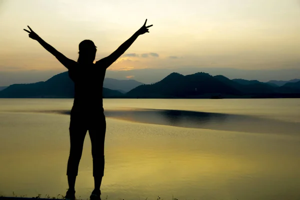 Silueta mujer feliz en el agua y las montañas al atardecer . — Foto de Stock