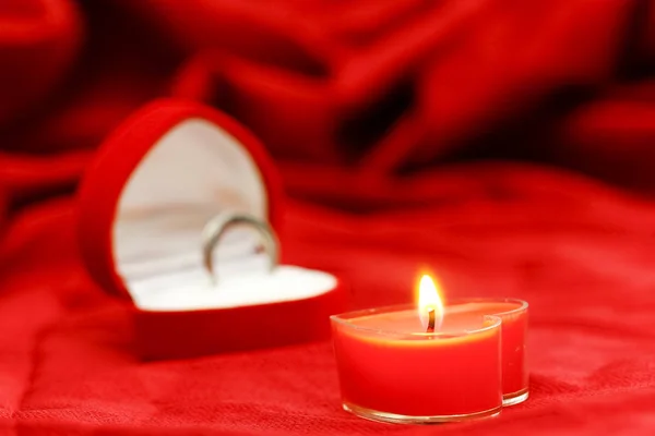 Одна свеча в форме сердца на красном шелковом фоне — стоковое фото