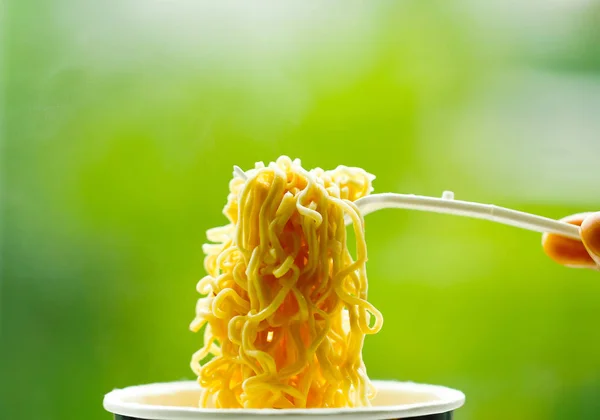 Fideos instantáneos en tazón con tenedor de plástico sobre fondo verde —  Fotos de Stock