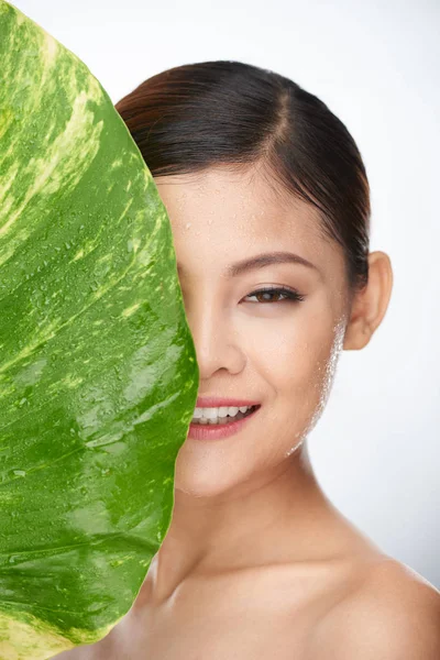 Kvinna som täcker hälften av ansiktet med gröna blad — Stockfoto