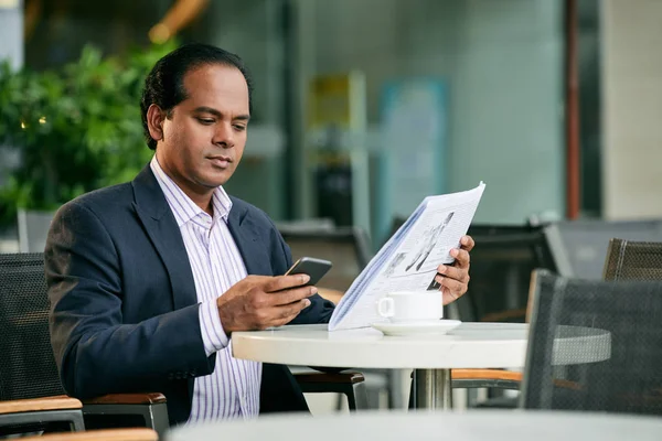 Businessman with newspaper and smartphone in cafe — Stock Photo, Image