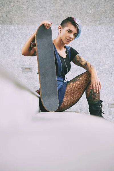 Жінка з скейтбордом дивиться на камеру — стокове фото