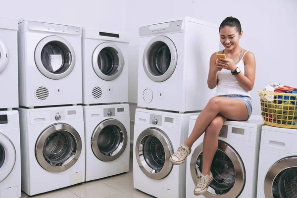 Chica sentada en la lavadora y mensajes de texto —  Fotos de Stock