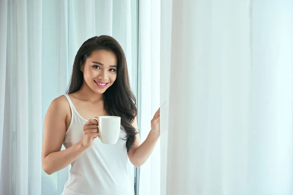 Жінка з чашкою кави, що стоїть біля вікна — стокове фото