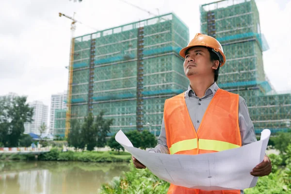 Bauunternehmer mit Bauplan betrachtet Gebäude — Stockfoto