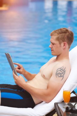 Yüzme Havuzu tarafından dinlenme süre tablet kullanarak genç adam yan görünüm