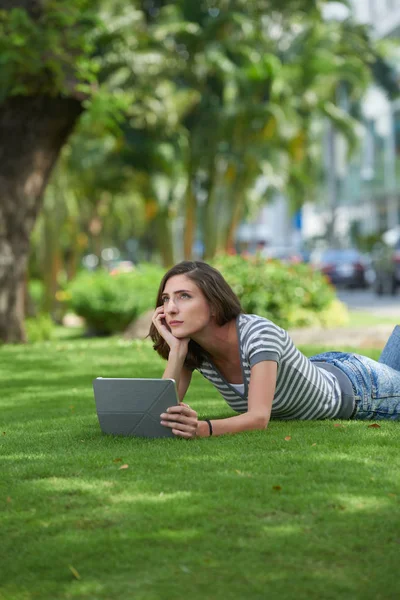 Девушка с планшетным компьютером лежит на траве — стоковое фото