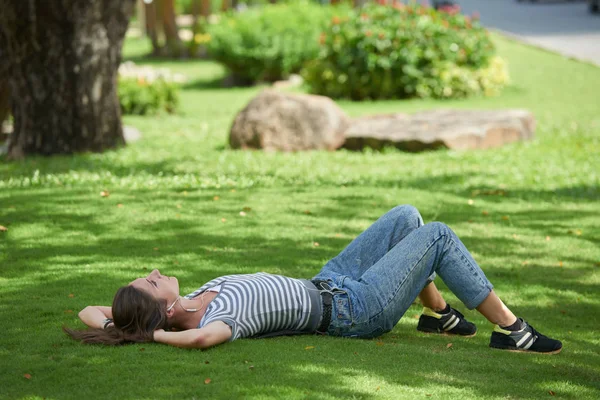 Vrouw liggen op gras in oortelefoons — Stockfoto