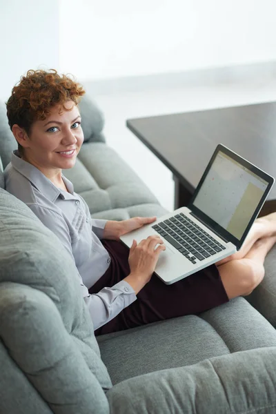 Жінка використовує ноутбук і лежить на дивані — стокове фото