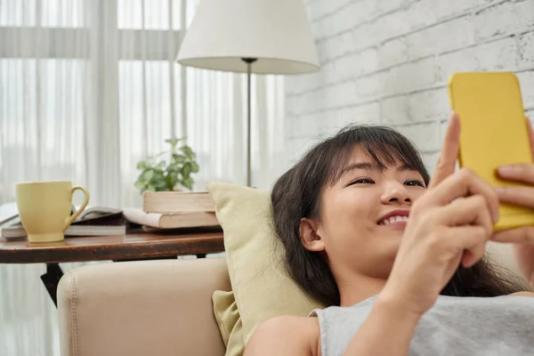 Mädchen liegt auf Sofa und benutzt Smartphone — Stockfoto