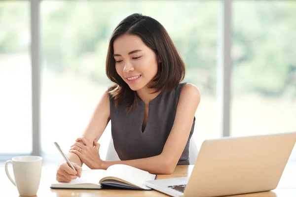年轻的亚洲商务妇女坐在桌子上 写在她的记事本 — 图库照片