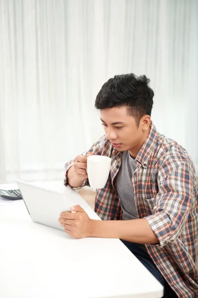 大きなカップにコーヒーを飲んだり デジタル タブレットのニュースを読んで若いアジアの男 — ストック写真