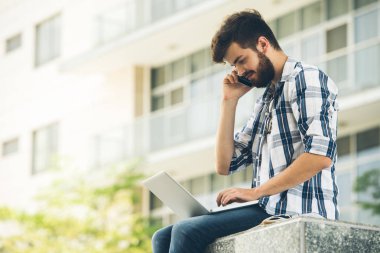Smartphone üzerinde arama ve dizüstü bilgisayar ekranında veri okuma genç adam