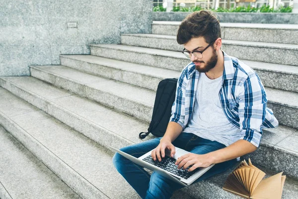 学生がキャンパスでの手順の上に座ってするときコンピューターに取り組んで — ストック写真