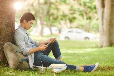 Dijital tablet kullanarak ağacın altında oturup ve okul projesi üzerinde çalışan emin Asya öğrenci