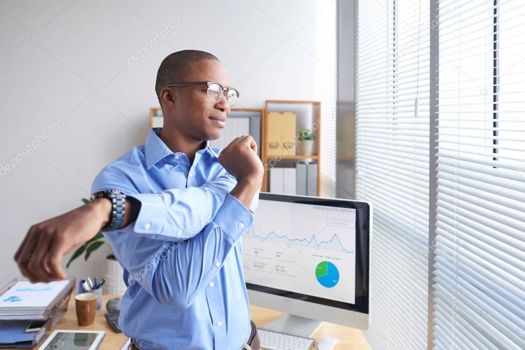 Smiling Black business executive stretching his arms during little break
