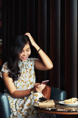 Smartphone cep telefonu ile bir şey okurken gülümseyen güzel Vietnamca genç kadın