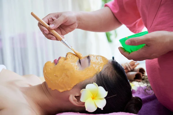 美容師は女性のクライアントの顔に保湿マスクを適用します — ストック写真