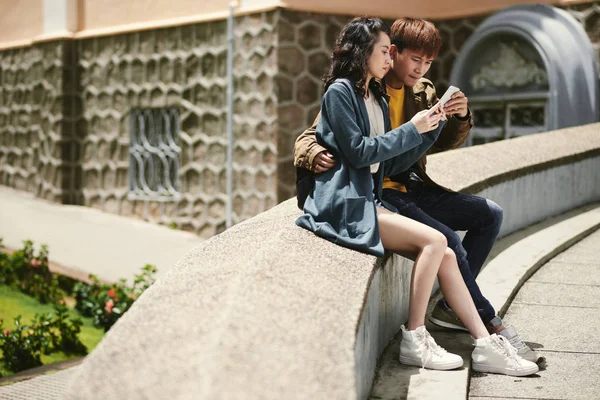 屋外に座っているベトナムのカップルを抱き締めると スマート フォンのアプリケーションを使用して — ストック写真