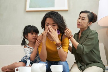 Crying Vietnamese woman being reassured by her daughter and senior mother clipart