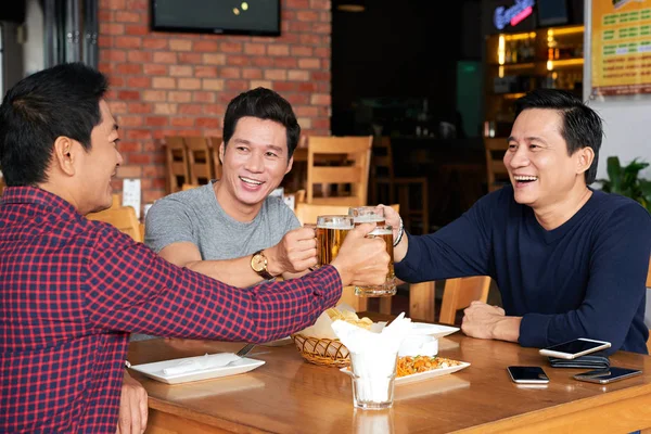 Group of happy middle-aged men drinking beer and talking in bar