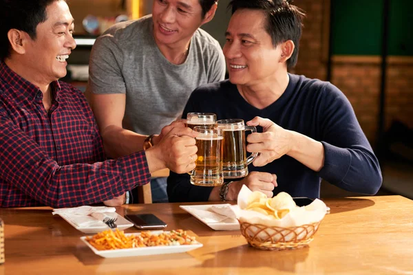 Laughing male friends toasting with beer mugs