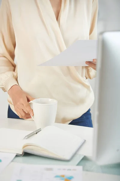 Middle section of businesswoman holding document and white tea mug in her hands
