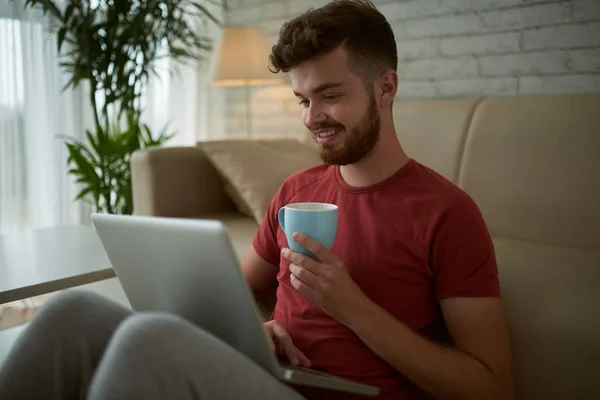 Улыбающийся Молодой Человек Чашкой Кофе Смотрит Видео Ноутбуке — стоковое фото