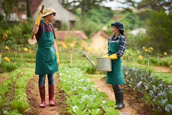 若いアジアの労働者からの短い休憩を取っている間ゴム長靴とエプロンを着て疲れる家庭菜園での作業 — ストック写真