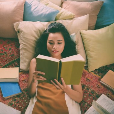 Çalışkan kız öğrenci bir kitapla yatakta yalan