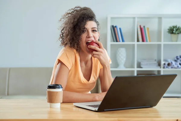 Mujer Rizada Joven Comiendo Manzana Roja Trabajando Ordenador Portátil — Foto de Stock