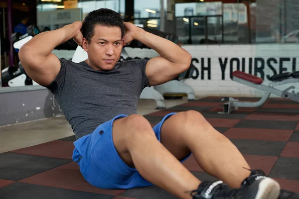 Vietnamese young man doing sit-ups on the gym floor
