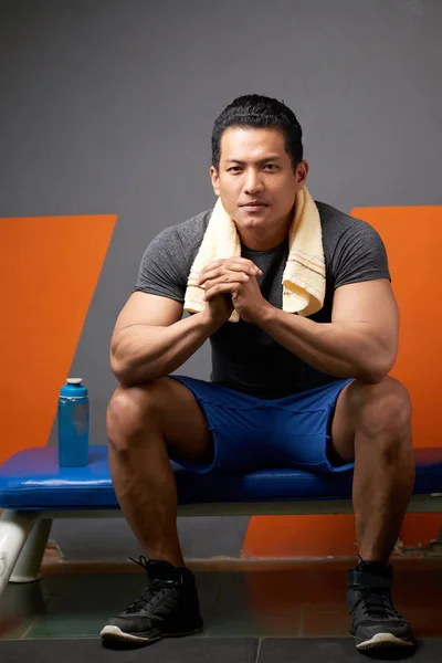 Portrait of Asian gym trainer sitting on bench with towel on his neck