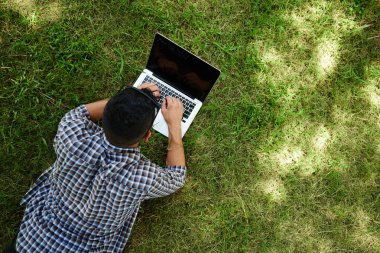 Dostum yeşil çim üzerinde yalan ve dizüstü bilgisayar, çalışma görüntülemek yukarıdan