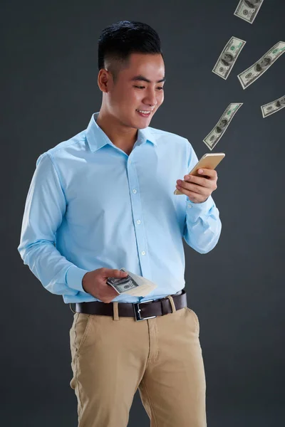 快乐的亚洲商人使用智能手机与美元票据出来的 — 图库照片