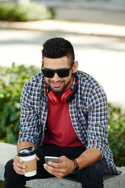 Portret Uśmiechający Się Młody Człowiek Słuchawki Picia Kawy Przeglądania Telefonie — Zdjęcie stockowe