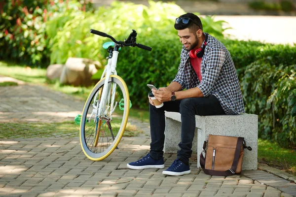 Joven Sonriente Sentado Banco Junto Bicicleta Comprobando Smartphone —  Fotos de Stock