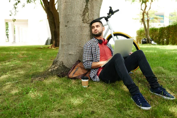 Zamyślony Młodzieniec Siedział Trawie Pod Drzewem Gdy Laptop Kolanach — Zdjęcie stockowe